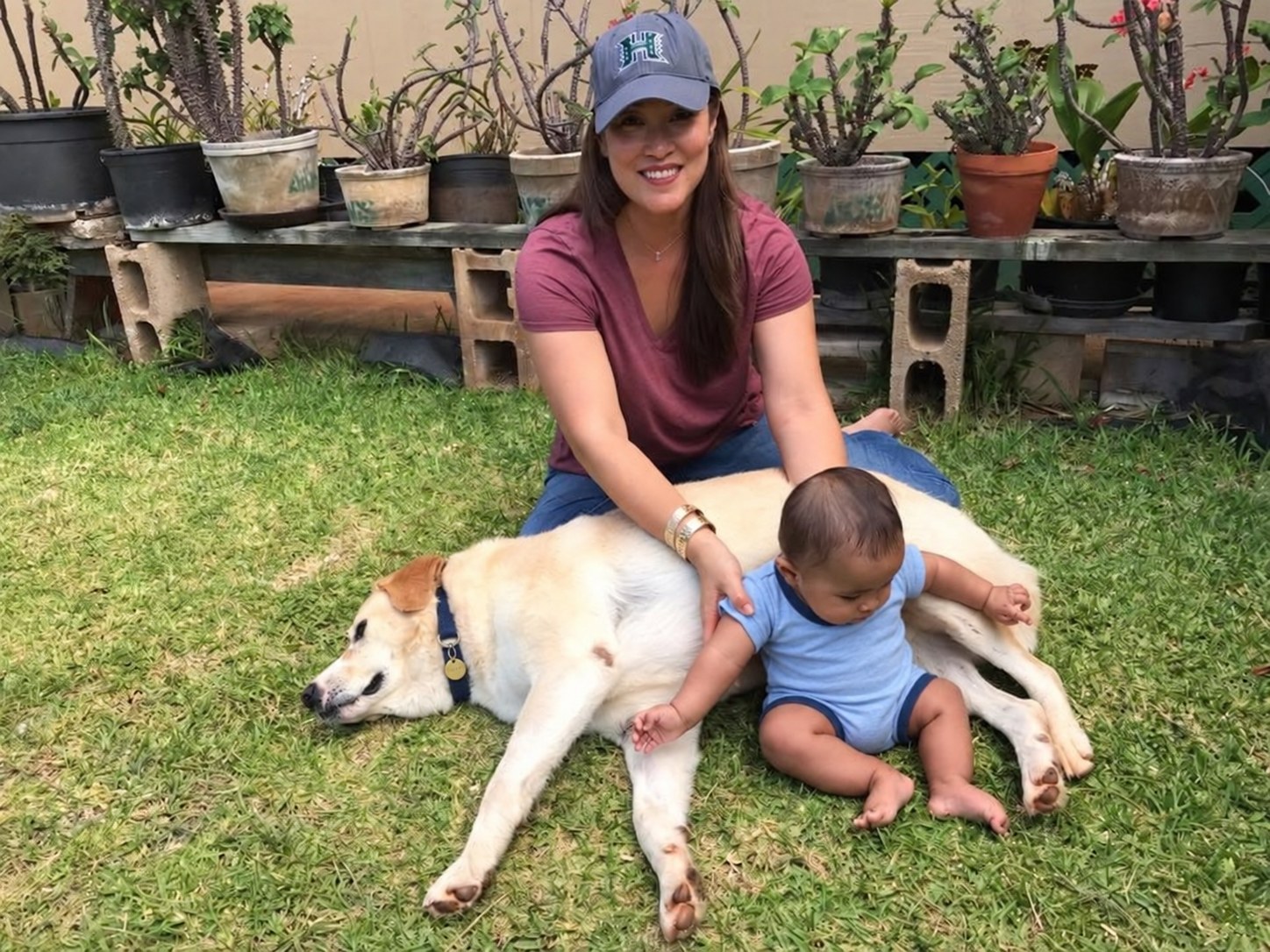 Pedro resting in the grass beside Gina and baby Krystian in Hawaiʻi